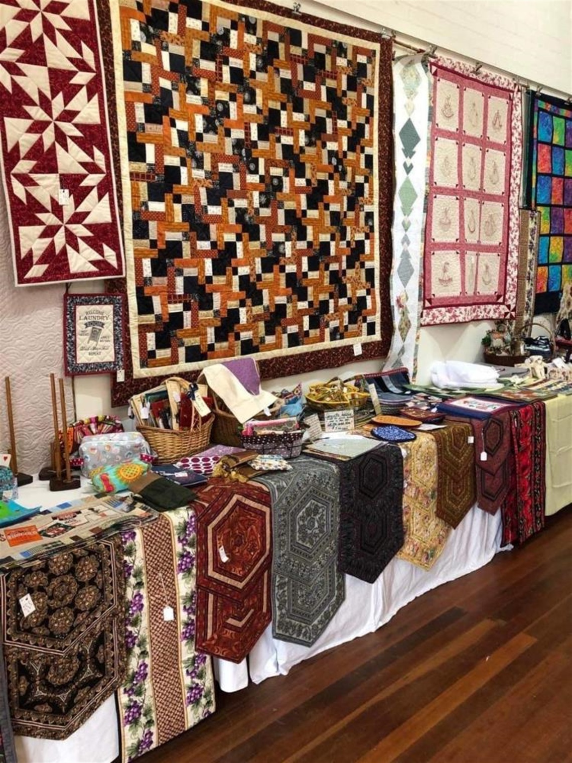 Handmade quilted items displayed on tables and gallery wall 