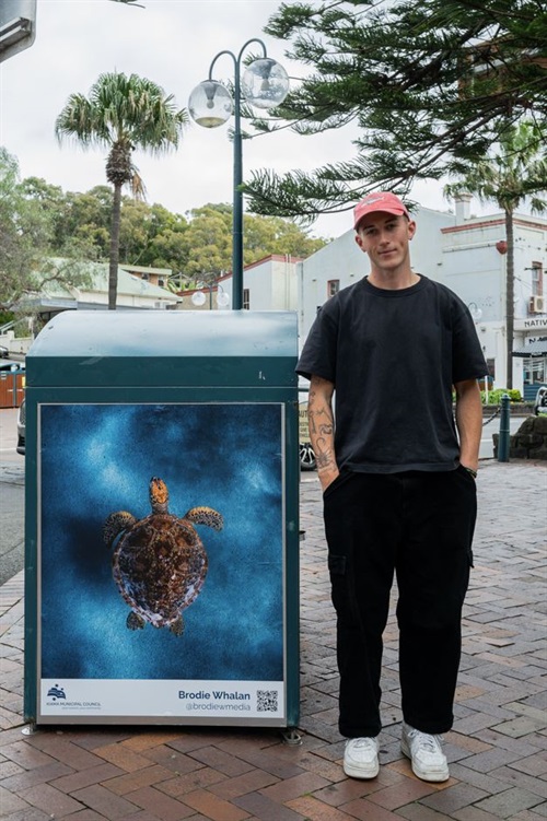 Artist standing near artwork featuring a turtle in the ocean 