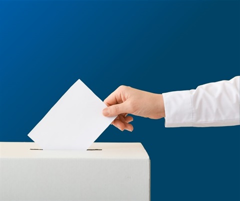 Mens hand placing a piece of white paper into a white cardboard ballot box. Blue gradient background